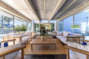 A modern living room with a large window, a central coffee table, and a view of a pool and outdoor area.