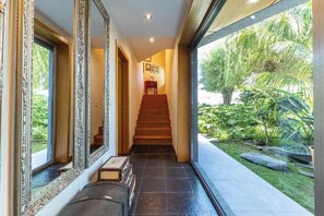 A hallway with a staircase leading to a room, large mirrors, and a view of greenery outside.