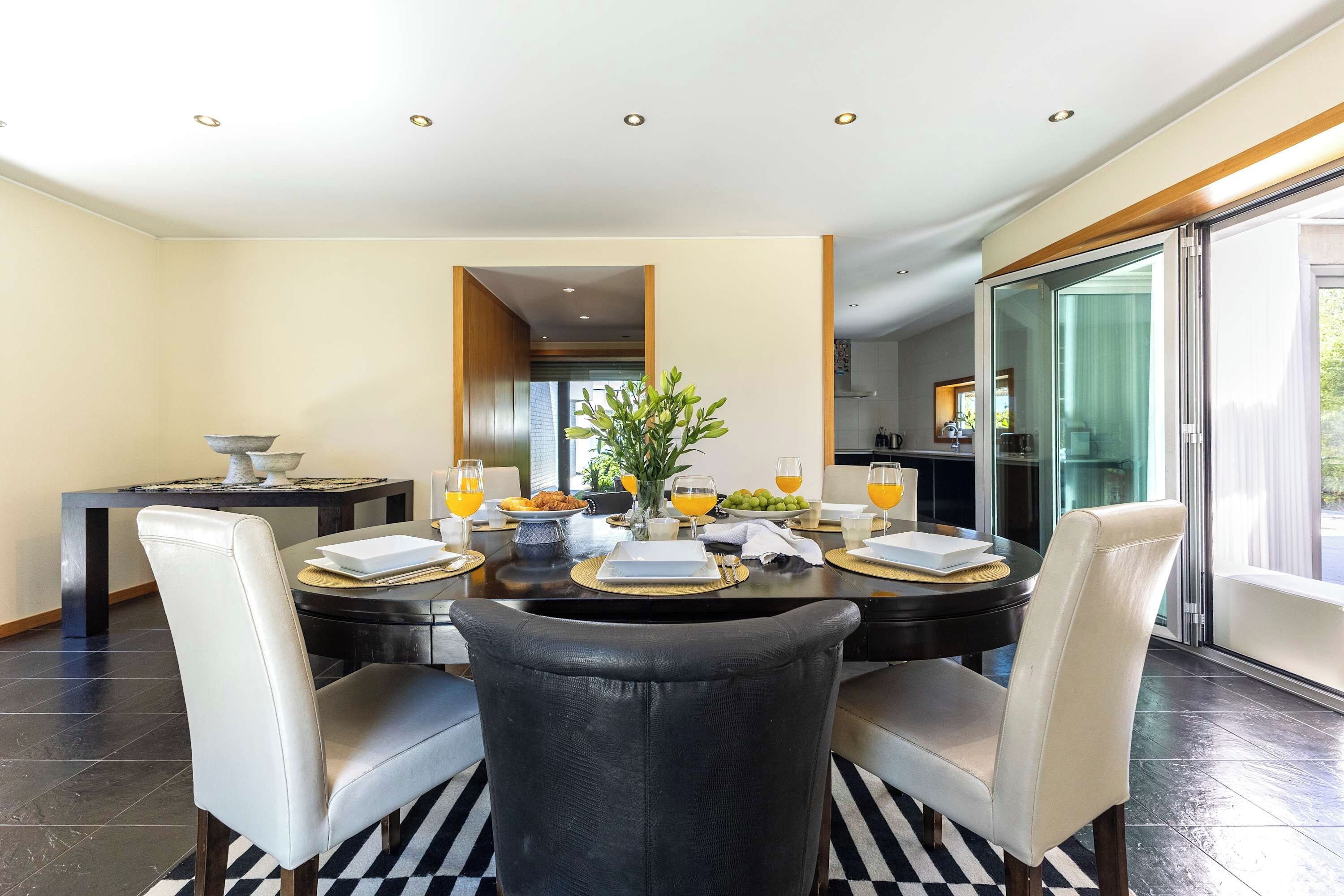 A dining area with a round table, four chairs, and a vase with flowers.