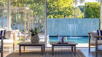 Zona de piscina con vistas a una pared azul de mosaicos, una mesa de madera con una planta y dos sofás blancos con cojines azules.