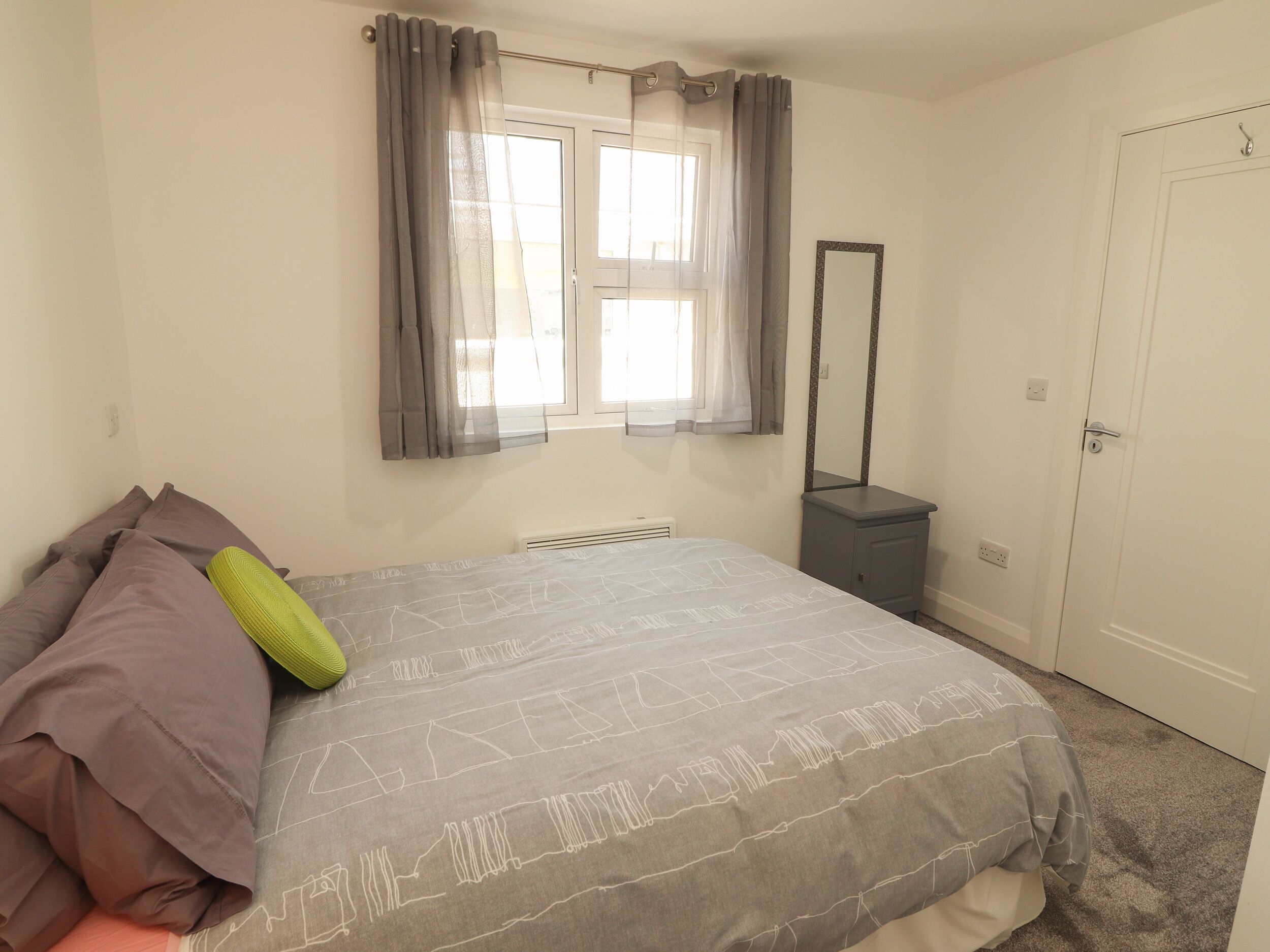 A bedroom with a bed, a window with curtains, a mirror, and a door.