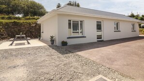 Een gelijkvloers huis met een witte gevel, een grindpad en een klein terras met een tafel en plantenpotten.