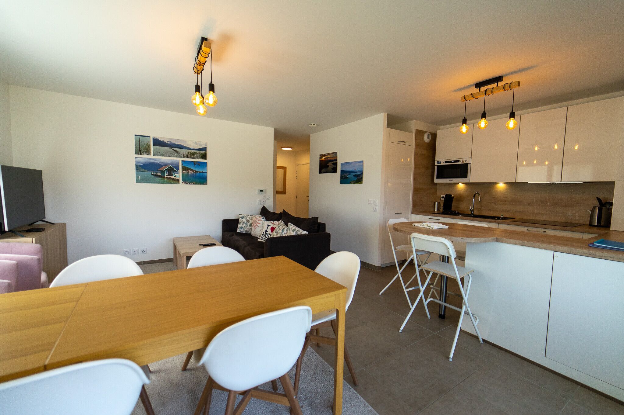 A modern kitchen with white cabinets, a wooden countertop, and a built-in microwave. There is a dining area with a wooden table and white chairs.