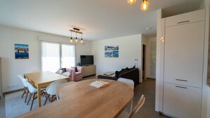 A modern living room with a wooden dining table, white chairs, a sofa, and a TV. There are light fixtures above the table and a white cabinet to the right. - La Douce Folie - Apartment for 4 to 5 people in Sevrier (Sévrier)