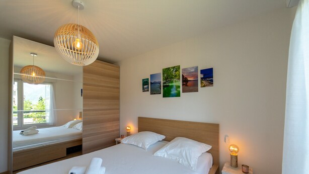 A neatly made bed with white linens and pillows, a bedside table with a lamp, and a wall with framed pictures. - La Douce Folie - Apartment for 4 to 5 people in Sevrier (Sévrier)