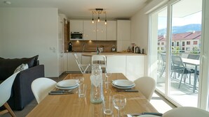 A modern kitchen with white cabinets, a wooden dining table set for four, and a view of a mountain landscape through large windows. - La Douce Folie - Apartment for 4 to 5 people in Sevrier (Sévrier)