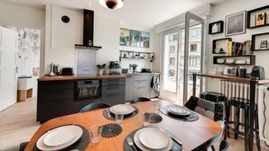 Una cocina moderna con comedor, que incluye una mesa de madera dispuesta para cuatro personas, horno empotrado y un ventanal que proporciona luz natural.