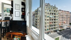 Una sala de estar moderna con un televisor grande, cuadros enmarcados y vista a un edificio de varios pisos.