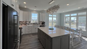 A modern kitchen with white cabinetry, a large island, and a view of the outdoors through large windows. - Custom 3BR 3BA with Private Pool & Elevator - new in 2022 (Sunset Beach)