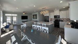 A spacious living area with a dining table, white chairs, a sofa, and a TV. - Custom 3BR 3BA with Private Pool & Elevator - new in 2022 (Sunset Beach)