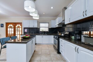 A modern kitchen with white cabinets, a central island, and a black backsplash. - 3BR Villa w/ Private Pool near Palm Beach (Noord)