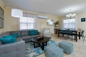 A living room with a grey sofa, a round coffee table, and a dining area with a table set for four.