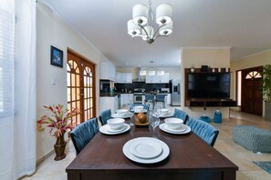 A dining area with a wooden table set for four, a chandelier, and a kitchen in the background. - Villa Retreat: 3BR w Private Pool near Palm Beach (Noord)