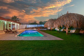 A swimming pool with lounge chairs and a thatched-roof structure. - 3BR Villa w/ Private Pool near Palm Beach (Noord)