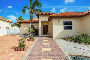 A residential property with a paved driveway, a front door, and a small garden area with plants and a palm tree.