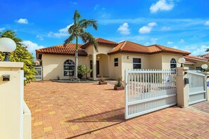 A residential property with a gated entrance, a paved driveway, and a palm tree. - Villa Retreat: 3BR w Private Pool near Palm Beach (Noord)