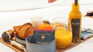 Ett frukostbricka med croissanter, apelsinjuice, en flaska apelsinjuice, ett glas apelsinjuice, ett glas marmelad, ett ljus och en bok med titeln "Palais des Thés".