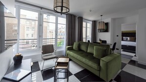 A modern living room with a green sofa, a dining table, and a chair. There is a large window with a view of buildings outside. - Quartier d'Hiver, 4 stars, Beautiful apartment close to the Champs-Elysées (París)