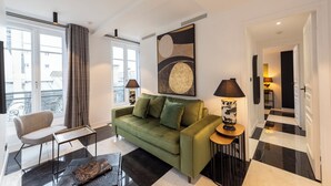 Una sala moderna con un sofá verde, un sillón estampado y una mesita de centro. Hay un cuadro abstracto grande en la pared y una lámpara sobre una mesita auxiliar.