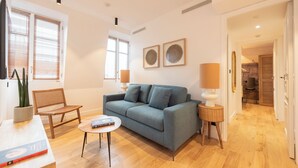 A modern living room with a grey sofa, a small round table, and a chair. There are two wall-mounted lamps and a potted plant. - Comte de Clare, 4 stars, Cosy apartment close to the Champs-Elysées (París)