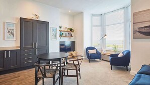 Uma sala de estar moderna com uma mesa de jantar de madeira escura, duas cadeiras, um sofá azul e uma televisão.