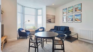 Uma sala de estar moderna com uma mesa redonda, sofás azuis e uma grande janela com persianas.