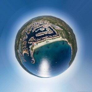 An aerial view of a coastal area with a marina, sandy beach, and residential buildings.