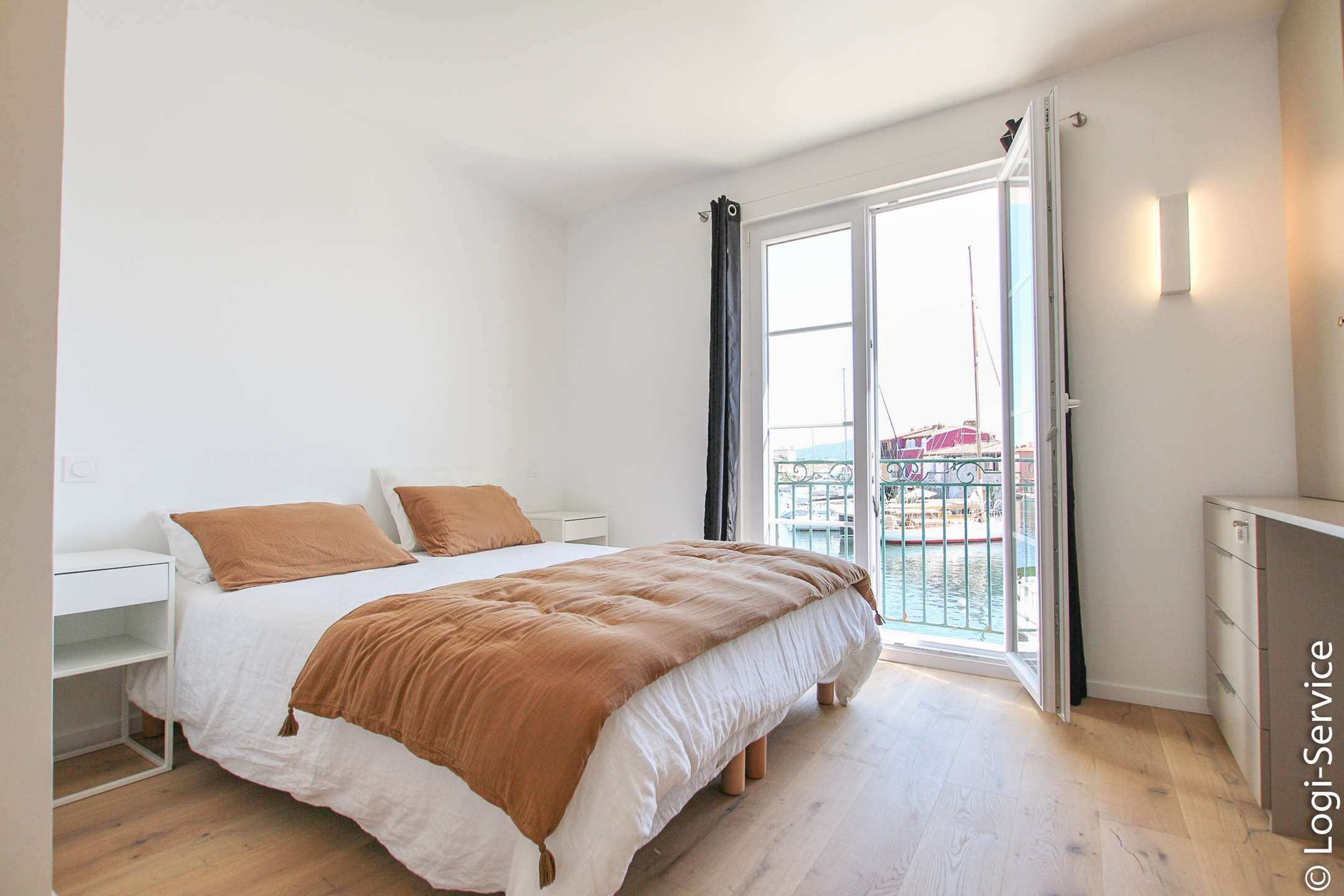 Ein Schlafzimmer mit Bett, Schreibtisch und einem Balkon mit Blick auf ein Gebäude.