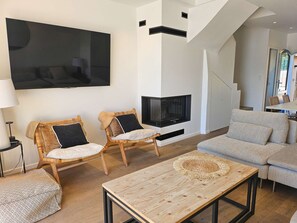 A modern living room with a flat-screen TV, two wicker chairs, a sofa, and a coffee table.
