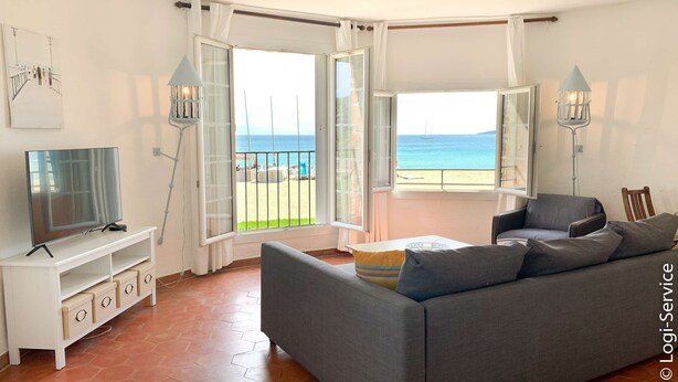 A living room with a sofa, TV, and a view of the beach. - On the beach 2 bedrooms flat 4/6 persons (PORT GRIMAUD)