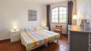 A bedroom with a bed, a chair, a desk, a window with curtains, and a lamp. - On the beach 2 bedrooms flat 4/6 persons (PORT GRIMAUD)