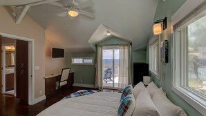 A bedroom with a bed, a desk, a chair, a television, and a balcony with a view of the ocean. - Paradise Ocean View, 2Br/2Ba (Keaau)
