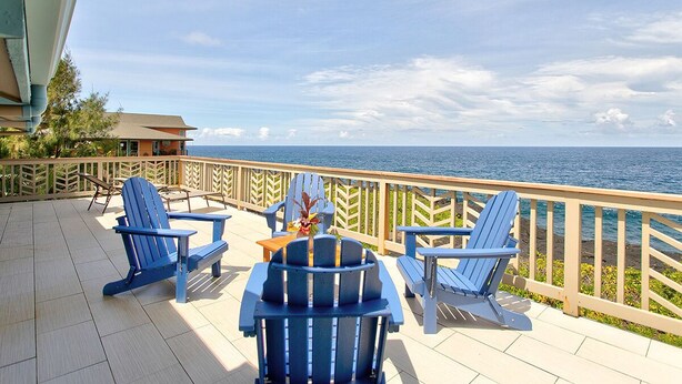 A deck with blue Adirondack chairs, a small table, and a view of the ocean. - Paradise Ocean View, 2Br/2Ba (Keaau)