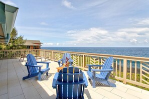 A deck with blue Adirondack chairs, a small table, and a view of the ocean. - Paradise Ocean View, 2Br/2Ba (Keaau)