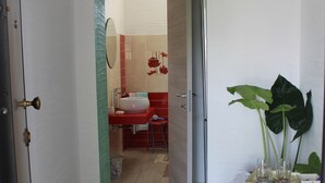 Un passadís que condueix a un bany amb un rentapans, un mirall i flors vermelles a la paret.