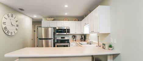 A modern kitchen with white cabinets, stainless steel appliances, and a central island with bar stools.