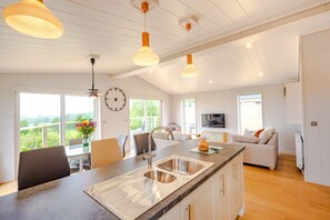 Uma cozinha espaçosa com uma ilha grande, luminárias pendentes modernas e vista para o exterior.