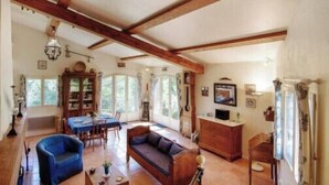 A spacious living area with a high ceiling, wooden beams, a dining table, a sofa, and a television. - Charming House In Garde Freinet With Garden (La Garde-Freinet)