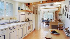 A kitchen with white cabinets, a wooden ceiling, and a dining area with a table set for two. - Charming House In Garde Freinet With Garden (La Garde-Freinet)