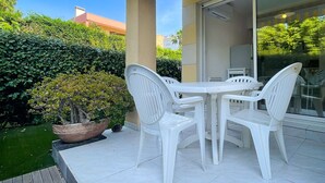 A patio with a white table and chairs, a potted plant, and a glass door leading to an indoor area.