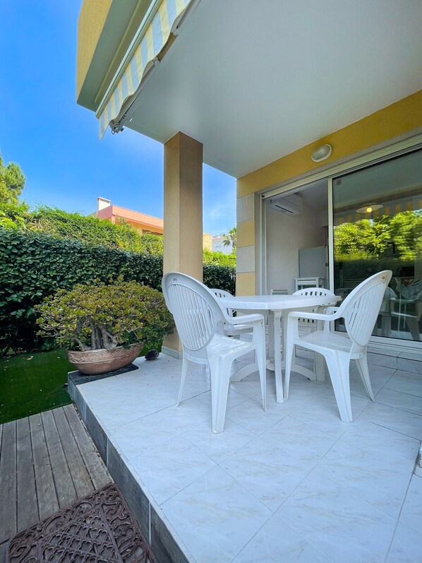 A patio with a white table and chairs, a potted plant, and a glass door leading to an indoor area.
