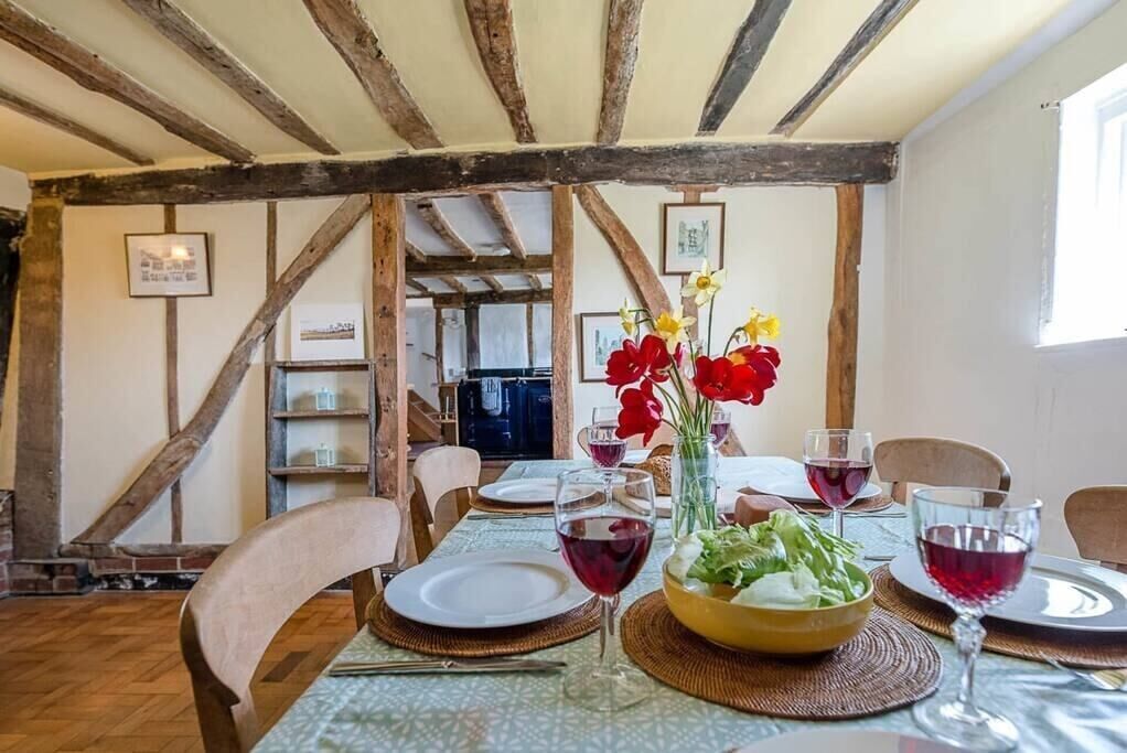 A dining area with wooden beams, a table set for four with wine glasses and a bowl of salad.