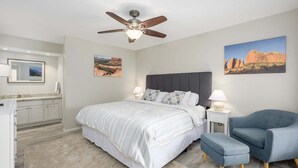 A bedroom with a bed, a nightstand, a chair, a ceiling fan, and two wall-mounted paintings. - Villa Stone Creek 2 Bedroom Condo by RedAwning (Scottsdale)