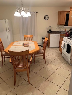 Uma cozinha compacta com mesa de jantar, cadeiras, geladeira, lava-louças, fogão e um relógio na parede.
