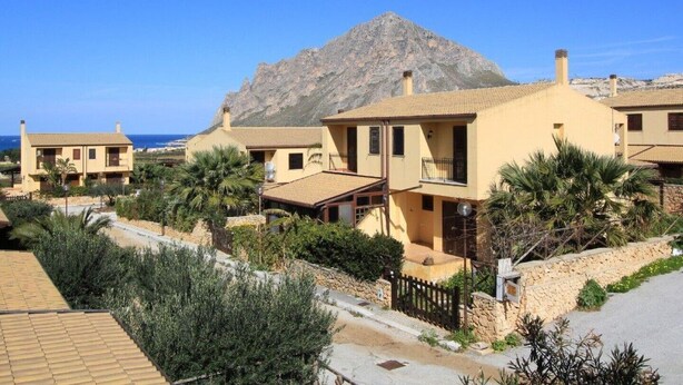 A residential area with houses featuring Mediterranean architecture, a stone wall, and a mountain in the background. - Casuzza di Gaia (Sicilia)