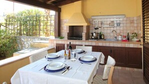 An outdoor dining area with a stone wall, a built-in grill, and a tiled backsplash. - Casuzza di Gaia (Sicilia)