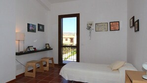 A room with two beds, a desk, a chair, and a small stool. There is a window with a view of buildings outside. - Casuzza di Gaia (Sicilia)
