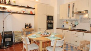 A compact kitchen with a round wooden table, white chairs, and a tiled floor. - Casuzza di Gaia (Sicilia)