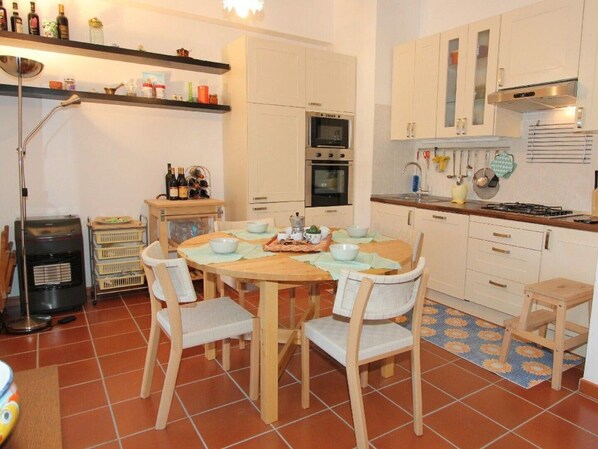 A compact kitchen with a round wooden table, white chairs, and a tiled floor.