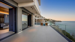 A modern balcony with a view of the sea, a glass door leading to a living area, and a dining setup with outdoor furniture. - Villa Nereid 5 bedroom villa with infinity heated pool (Rodia)